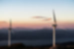 Two large wind turbines at sunset amidst a backdrop of mountains and low clouds